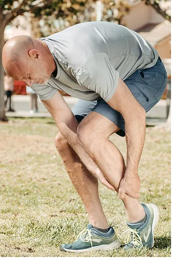 Ankle-sprain-Causes-Symptoms-and-Treatments
A man is outside, bending over in discomfort, holding his leg, possibly experiencing pain in his knee or shin area. He's dressed in activewear, suggesting he may have been exercising.