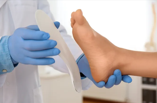 Custom-orthotics-types-uses-and-who-can-get-them- A healthcare provider in blue gloves is holding a foot and an orthotic insole, likely for fitting or assessment.