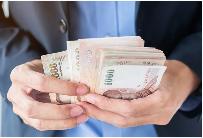 How-Much-Does-A-Chiropractor-Cost-Factors-That-Affect-Chiropractic-Cost someone in a business suit holding a stack of banknotes, suggesting a financial theme or the act of payment.