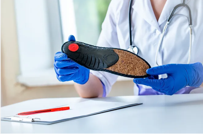 How-Often-do-I-Need-to-Replace-My-Custom-Orthotics- a healthcare professional wearing blue gloves, holding a custom orthotic shoe insert, likely during an evaluation or consultation.