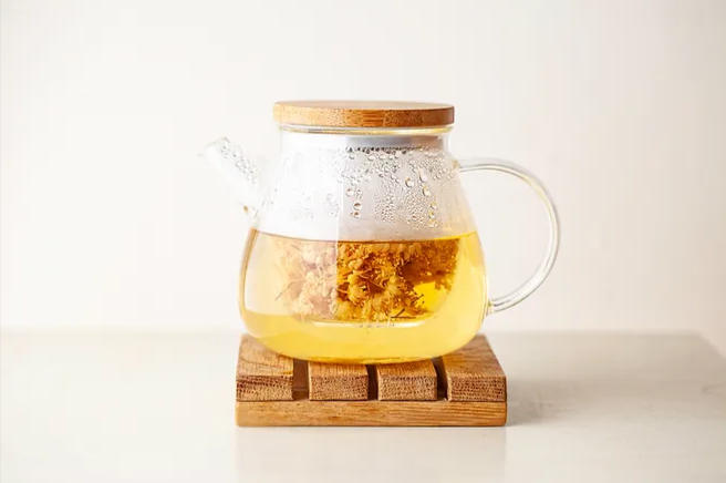 Types-of-Tea-That-May-Help-With-Weight-Loss-What-Teas-Aid-in-Burning-Fat- a glass teapot with a wooden lid, filled with golden-colored tea, resting on a wooden stand