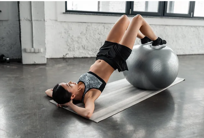a person performing an exercise on a gym ball, possibly focusing on core strength or stability, in a fitness studio setting.